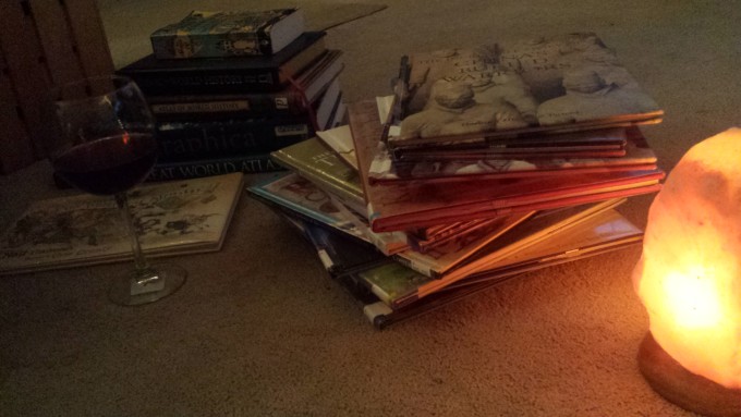 two piles of books, a lamp, and a glass of wine