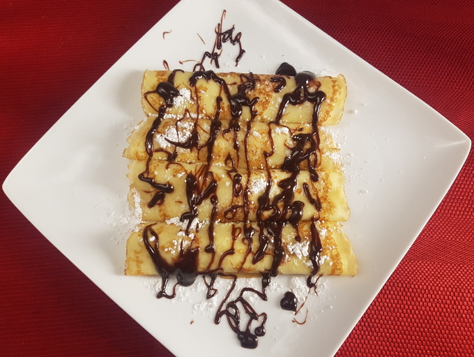 Crêpes stuffed with bananas and topped with powdered sugar and hot fudge